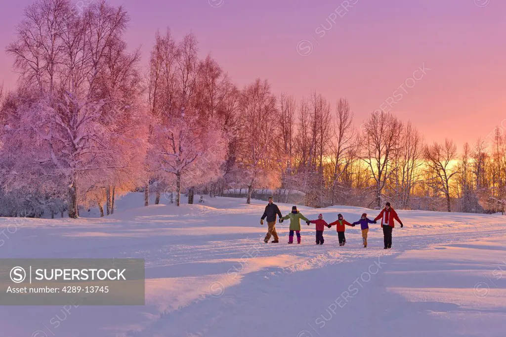 Family group, holding hands, walk on a snow path at sunset with a birch forest in the background, Russian Jack Springs Park, Anchorage, Southcentral A...