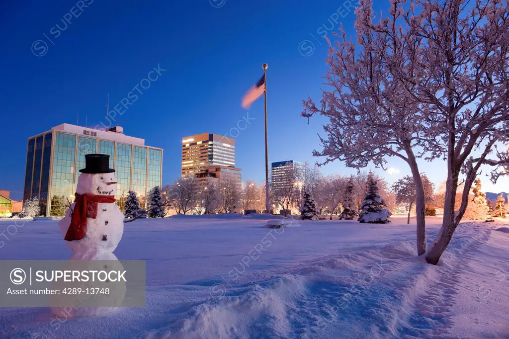 Snowman standing in Delaney Parkstrip with downtown Anchorage in the background at twilight, Southcentral Alaska, Winter. Digitally enhanced.