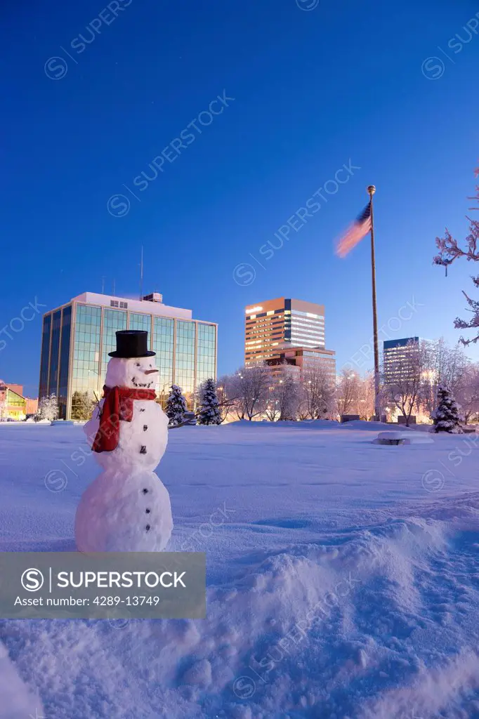 Snowman standing in Delaney Parkstrip with downtown Anchorage in the background at twilight, Southcentral Alaska, Winter. Digitally enhanced.