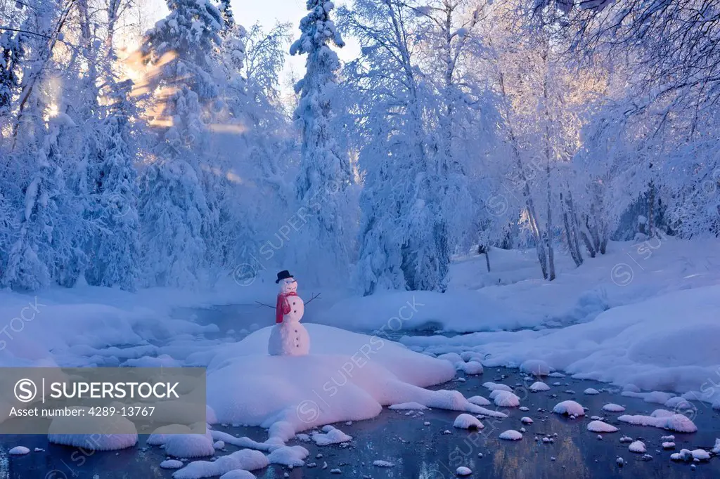 Snowman standing on a small island in the middle of a stream with fog and hoar frosted trees in the background, Russian Jack Springs Park, Anchorage, ...