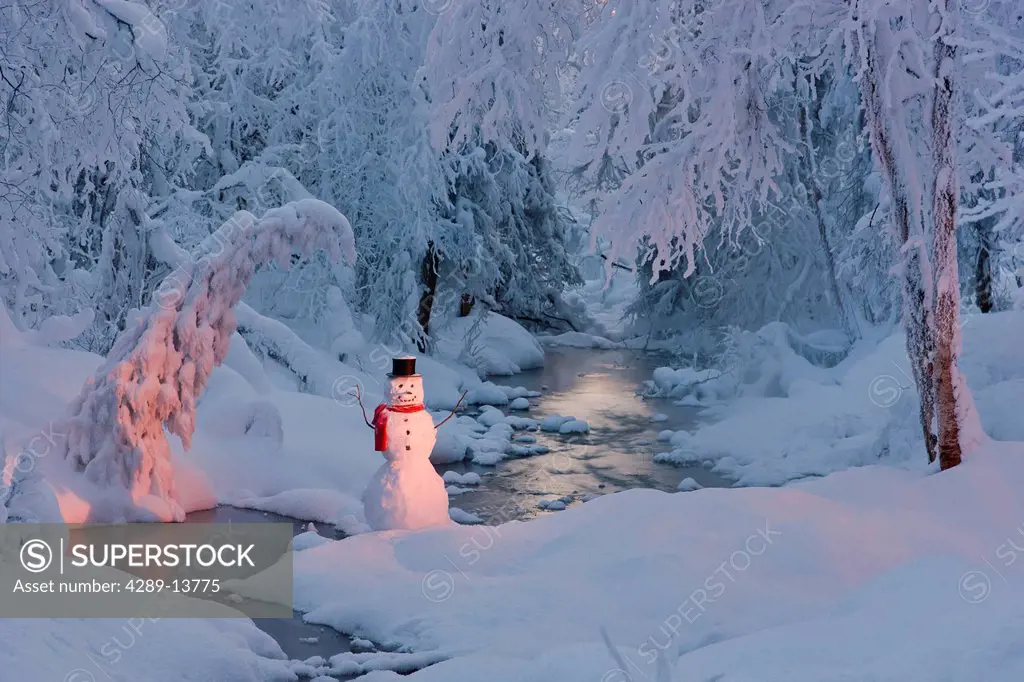 Snowman wearing a black scarf and top hat standing next to a small stream in a hoarfrost covered forest at twilight, Russian Jack Springs Park, Anchor...