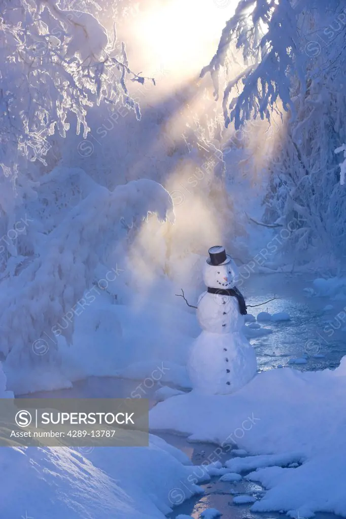 Snowman standing next to a stream with sunrays shining through fog and hoar frosted trees in the background, Russian Jack Springs Park, Anchorage, Sou...