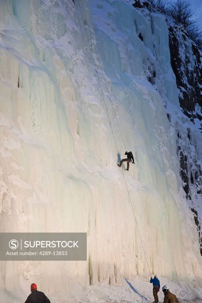 Evening light shines on an ice climber as he repels down an ice waterfall along Turnagain Arm, Southcentral Alaska, Winter