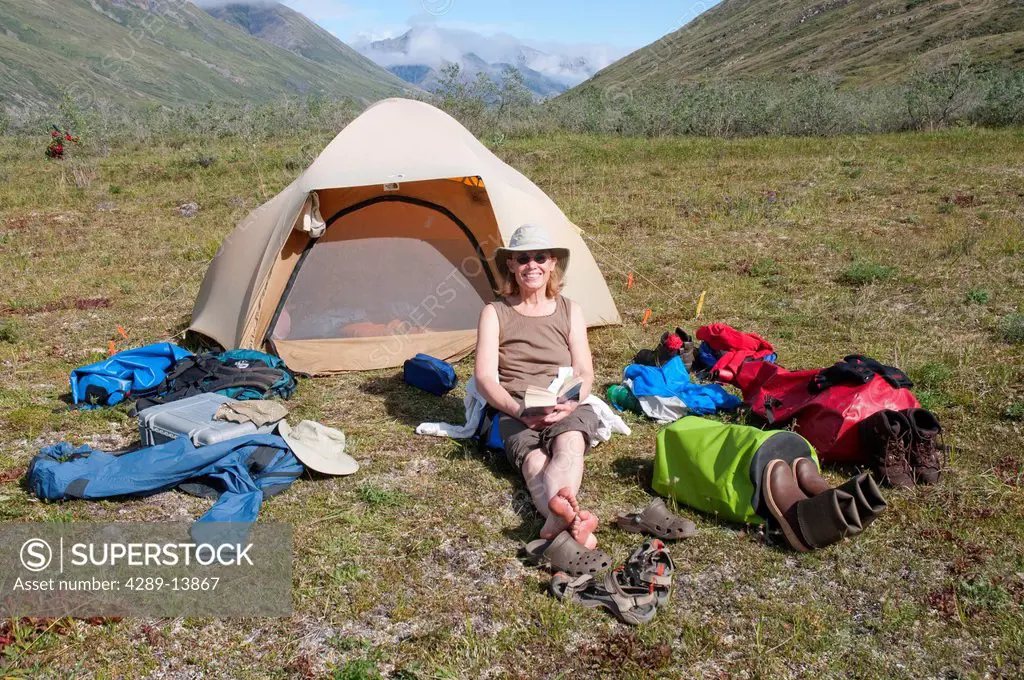 Mature female camper relaxes by tent on a sunny day on the Marsh Fork of the Canning River in the Brooks Range, Arctic National Wildlife Refuge, Alask...