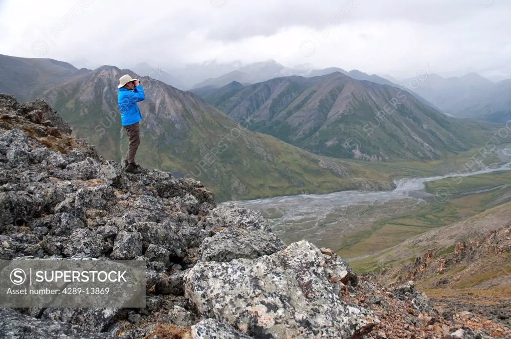 Mature female hiker on a rock glassing the landscape above the Marsh Fork of the Canning River in the Brooks Range, Arctic National Wildlife Refuge, A...
