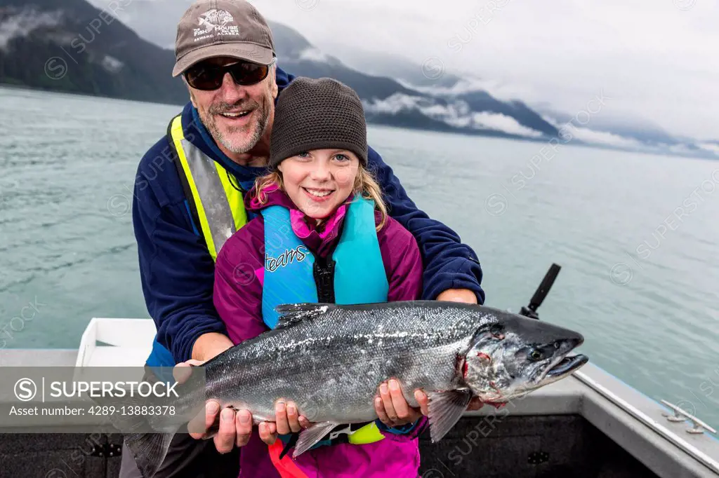Father and daughter holding up a Silver Salmon while on a boat, Seward, Southcentral Alaska, USA