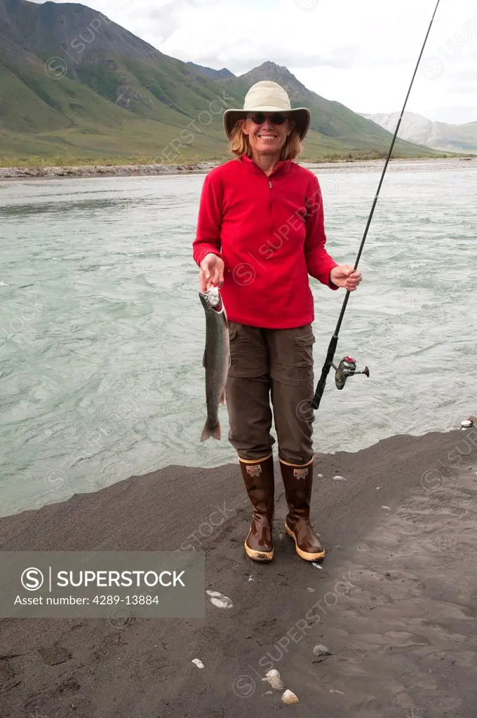 Mature woman squatting with fishing pole shows off Dolly Varden Char caught in the Canning River, Brooks Range, Arctic National Wildlife Refuge, Alask...