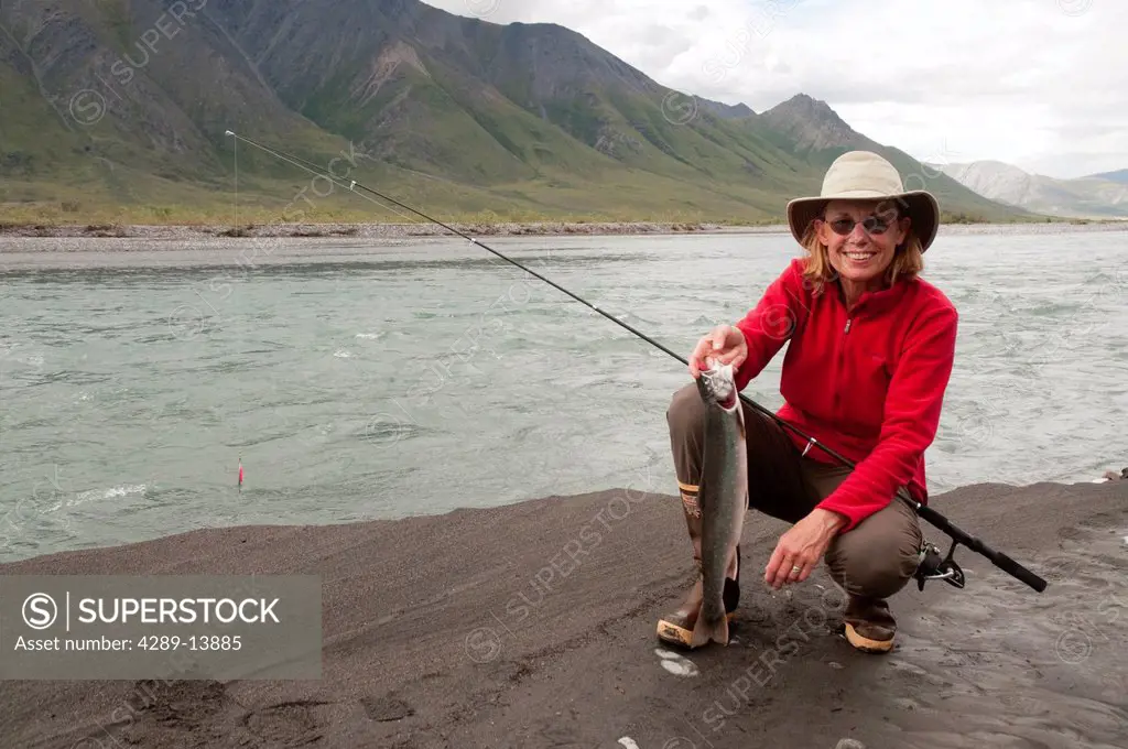 Mature woman squatting with fishing pole shows off Dolly Varden Char caught in the Canning River, Brooks Range, Arctic National Wildlife Refuge, Alask...