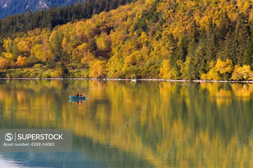 Fishermen in a small boat fish for salmon in Chilkoot Lake surrounded by fall colors reflected in the lake, Southeast Alaska