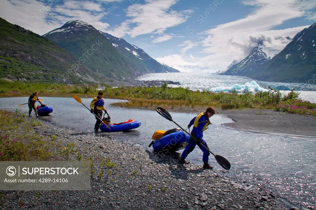 Three women pull their packrafts along the shore of Spencer Glacier Lake, Kenai Mountains, Southcentral Alaska, Summer