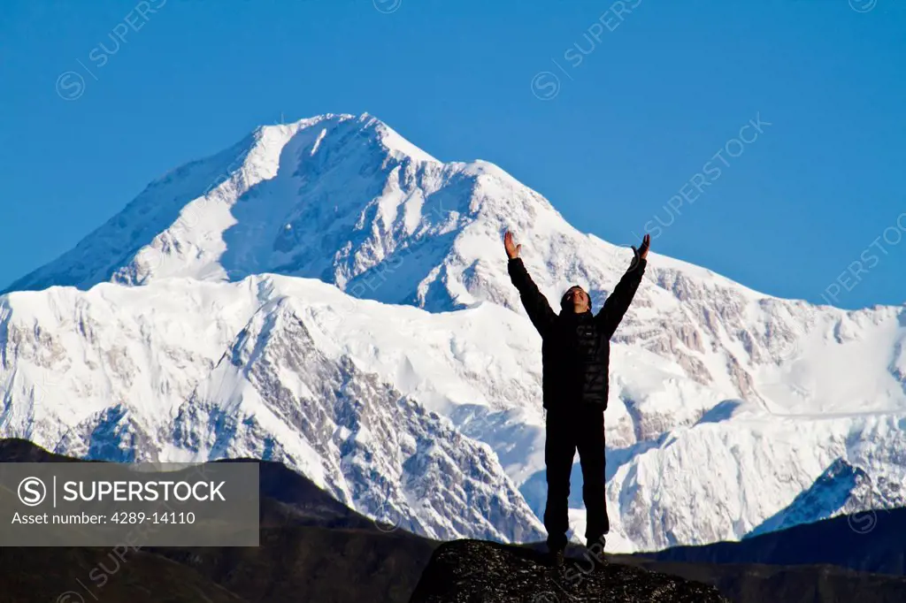 Silhouette of a man standing on Ruth Glacier with arms outstretched with Mt. McKinley in the background, Interior Alaska, Summer