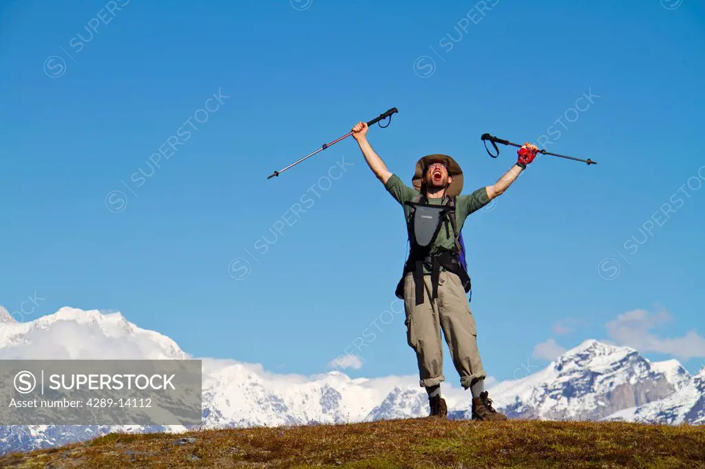 Man rejoicing with arms outstretched while hiking a tundra ridge between the Ruth Glacier and Tokositna Glacier, Denali National Park & Preserve, Inte...