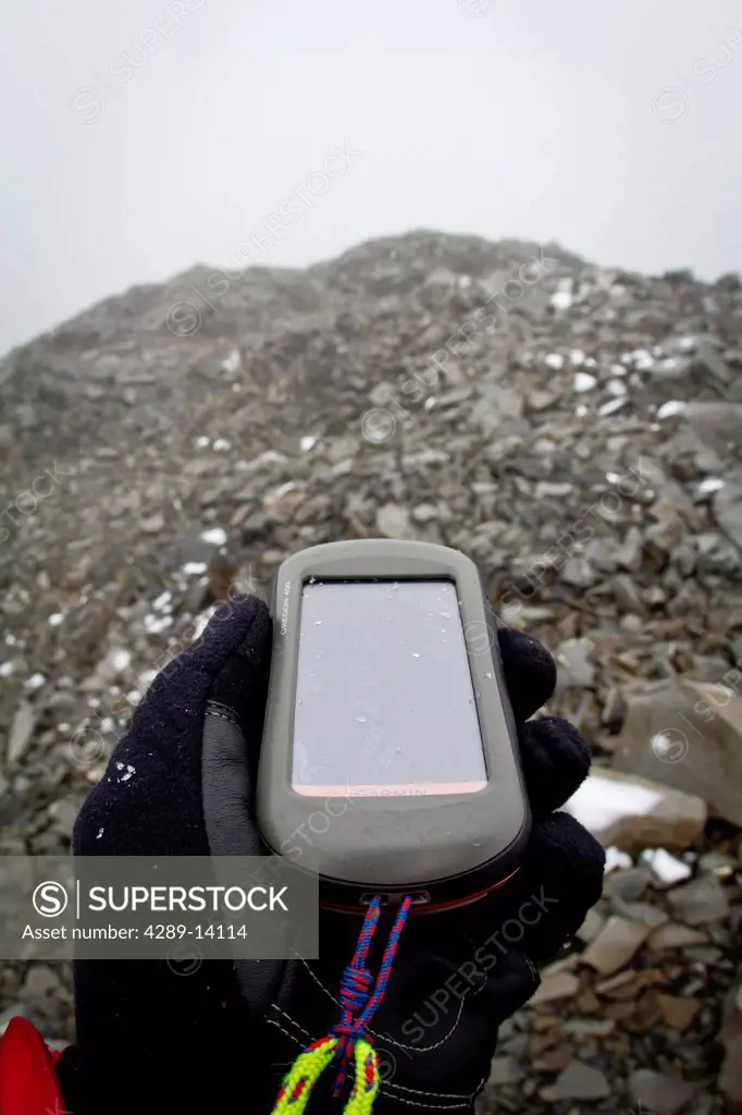 View of a hand holding a GPS and navigating a fog whiteout on a rocky ridge between the Ruth Glacier and Tokositna Glacier, Denali National Park & Pre...