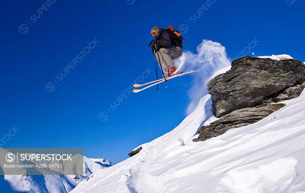 A skier jumps off a rock in Hatcher Pass and skiis downhill, Southcentral Alaska