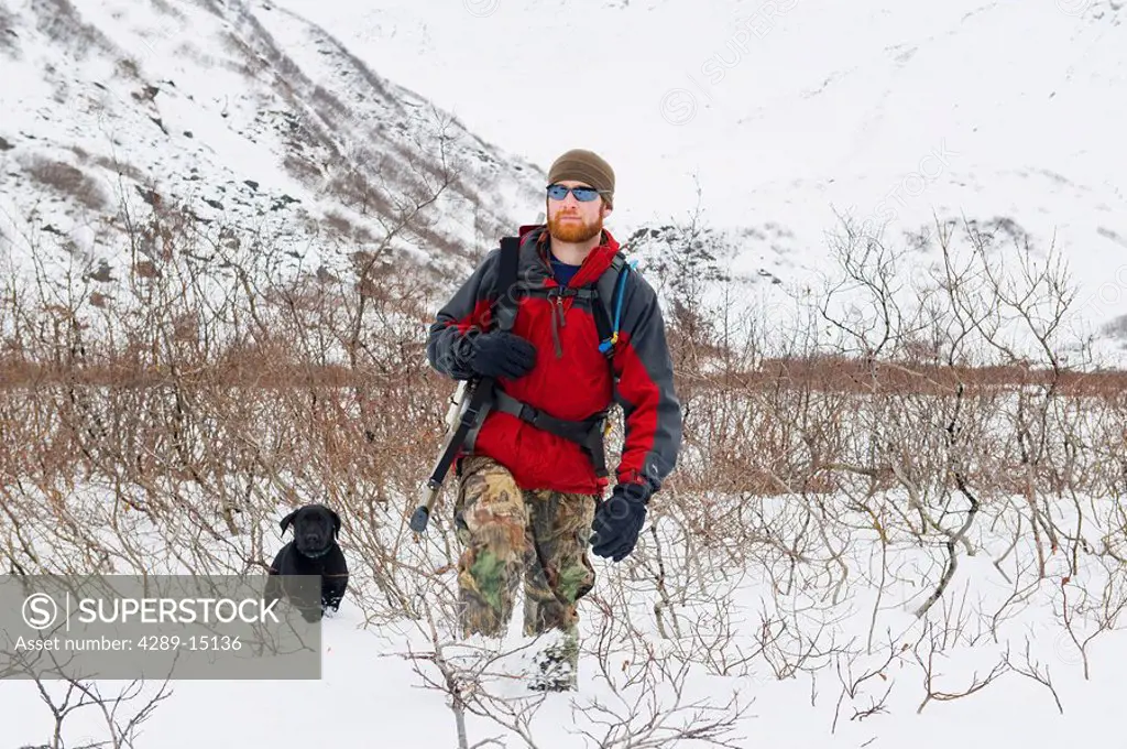 Man hunts for Ptarmigan with his black lab puppy and chocolate lab in Granite Basin near Juneau, Southeast Alaska during Winter