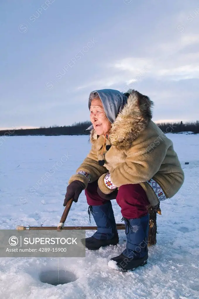 Elder native Yupik female sits on stump ice fishing Kuskokwim River Tuluksak Western Alaska Winter