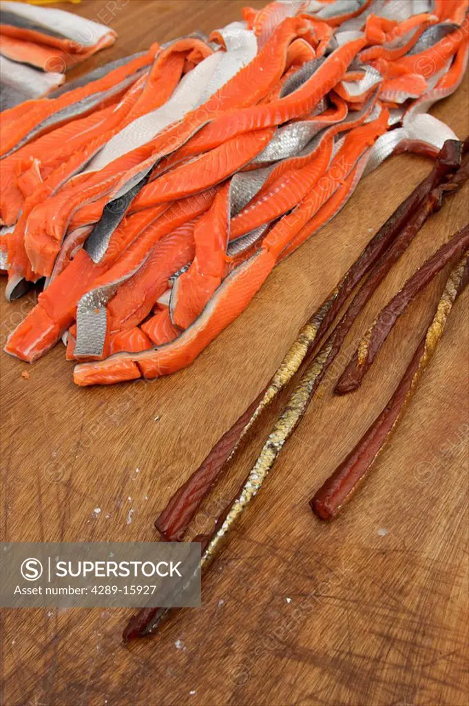 Close up of strips of freshly cut salmon next to the end product of dried salmon, Alaska