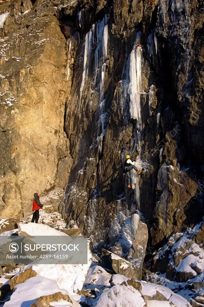 Man ice climbing while friend spots on frozen waterfall Turnagain Arm SC Chugach Mtns Winter Alaska