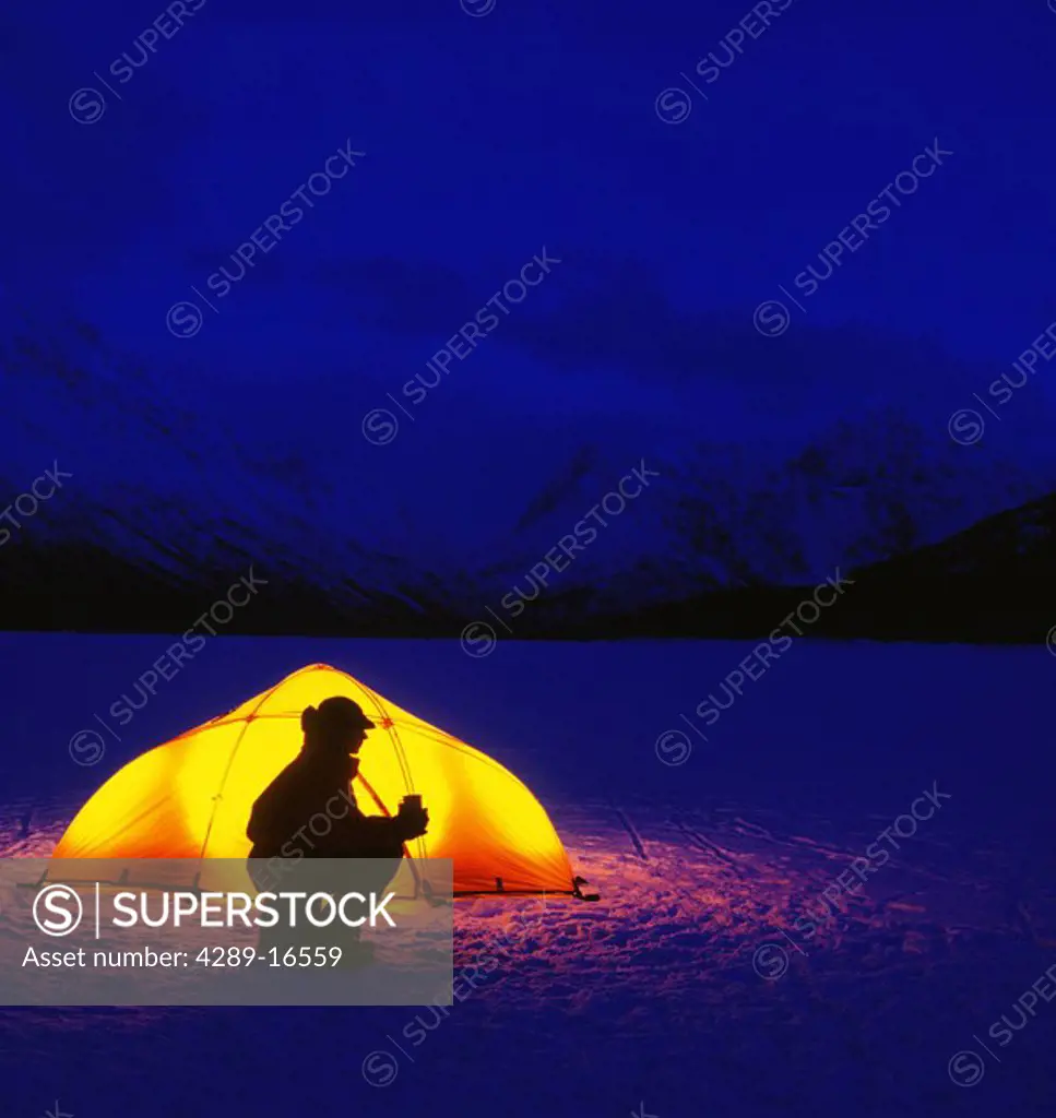 Woman silhouetted by lighted tent Eklutna Lake SC AK