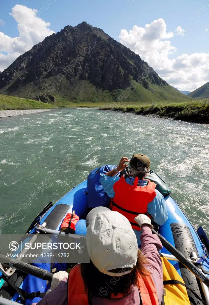 Two rafters rowing through a fast stretch of the Kongakut River on a sunny day with scenic mountains in the background, ANWR, Arctic Alaska, Summer