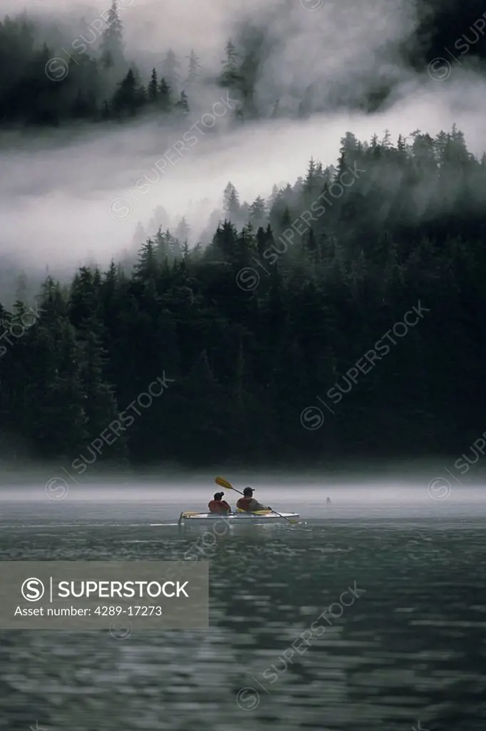 Couple sea kayaking in Red Bluff Bay w/mist rolling off Baranof Isl Chatham Strait Southeast Alaska