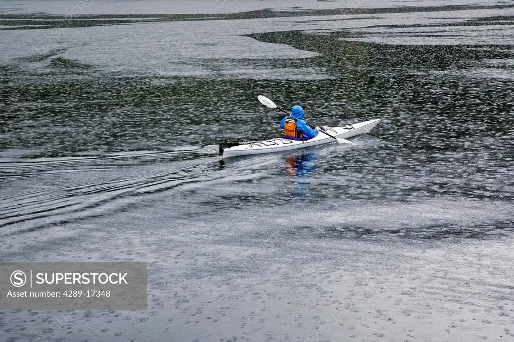 Sea kayaker paddling through rain squall Tracy Arm Fords_Terror Wilderness Area Southeast Alaska