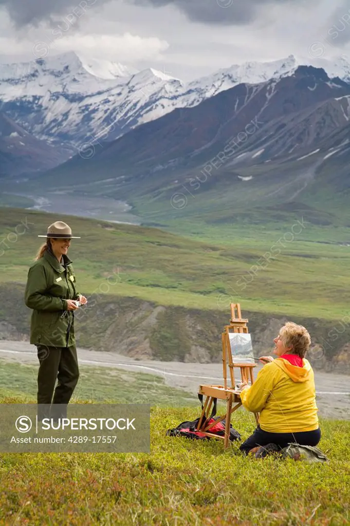 Female National Park Ranger talks with female oil painting artist who is sitting on tundra near Eielson Denali NP Alaska