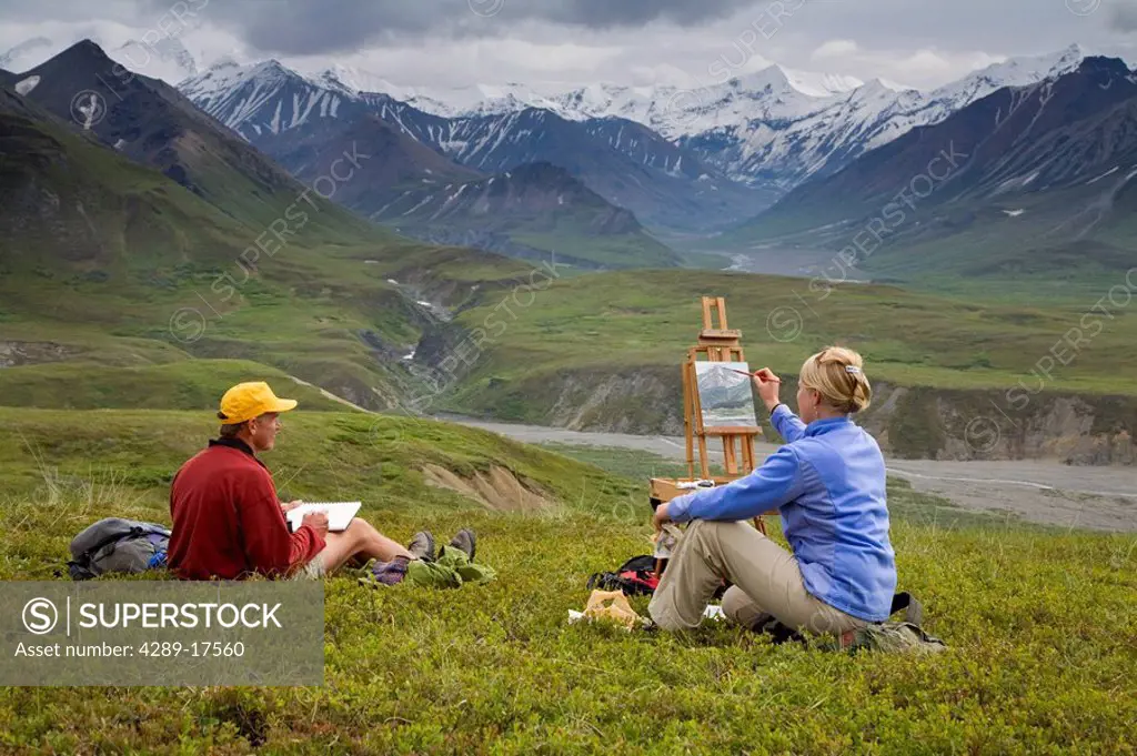 Male pencil sketch artist and female oil painting artist sitting on tundra painting the landscape Denali National Park Alaska