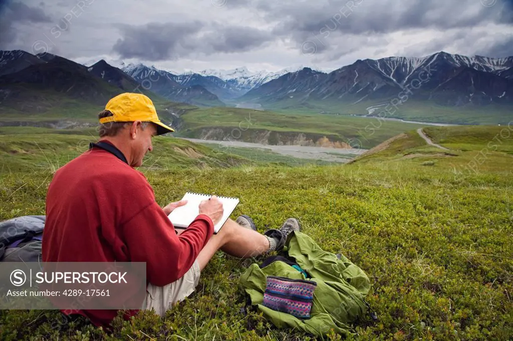Male pencil sketch artist and female oil painting artist sitting on tundra painting the landscape Denali National Park Alaska