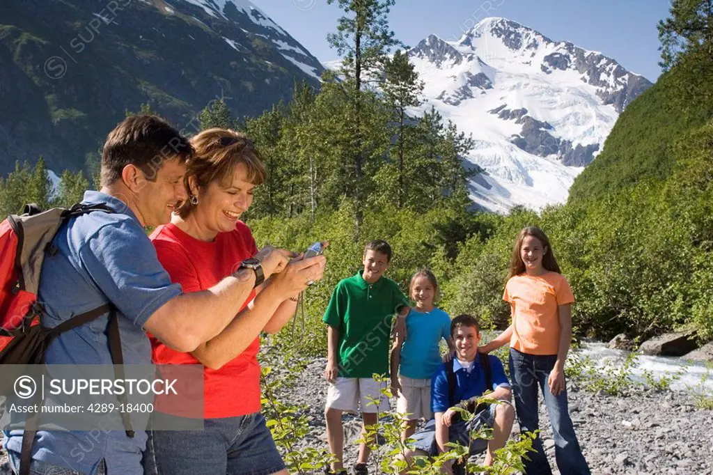 Mother and father review digital picture on camera with children in background while on hike to Byron Glacier Portage Chugach Nat Forest Southcentral ...