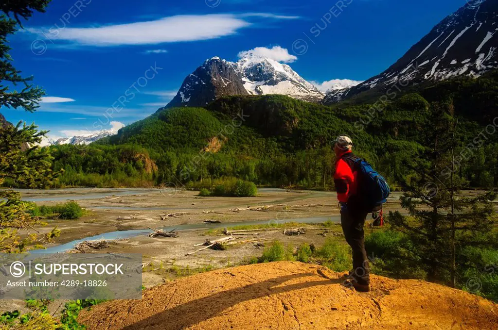 Hiker stands on a rock outcrop overlooking Eagle River, Chugach State Park, Southcentral Alaska, Summer