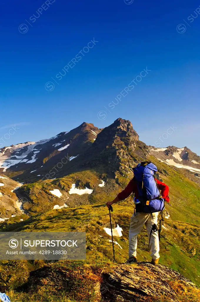 A man backpacking near Hatcher Pass in the Talkeetna Mountains with Bald Mountain Ridge in the background, Southcentral Alaska, Summer