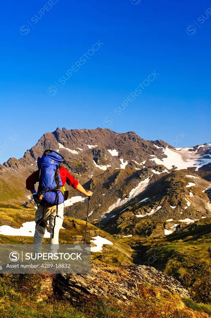 A man backpacking near Hatcher Pass in the Talkeetna Mountains with Bald Mountain Ridge in the background, Southcentral Alaska, Summer