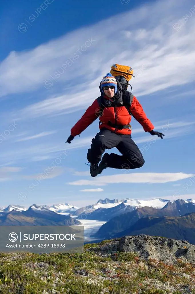 Male hiker with cell phone jumping in excitement on ridge above Inside Passage during Alaska Summer