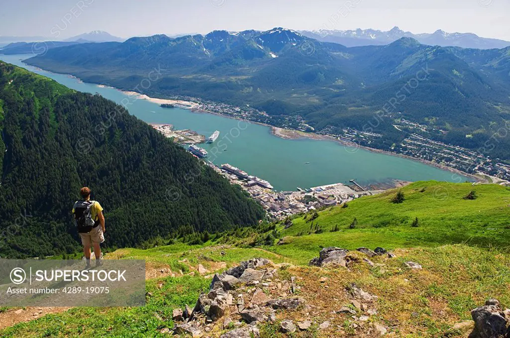A hiker takes in the view of Gastineau Channel, Douglas Island, and Downtown Juneau from the top of Mt. Juneau in Southeast Alaska during Summer
