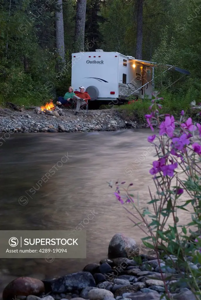 A couple enjoy their campfire near their travel trailer by Montana Creek in Southcentral Alaska