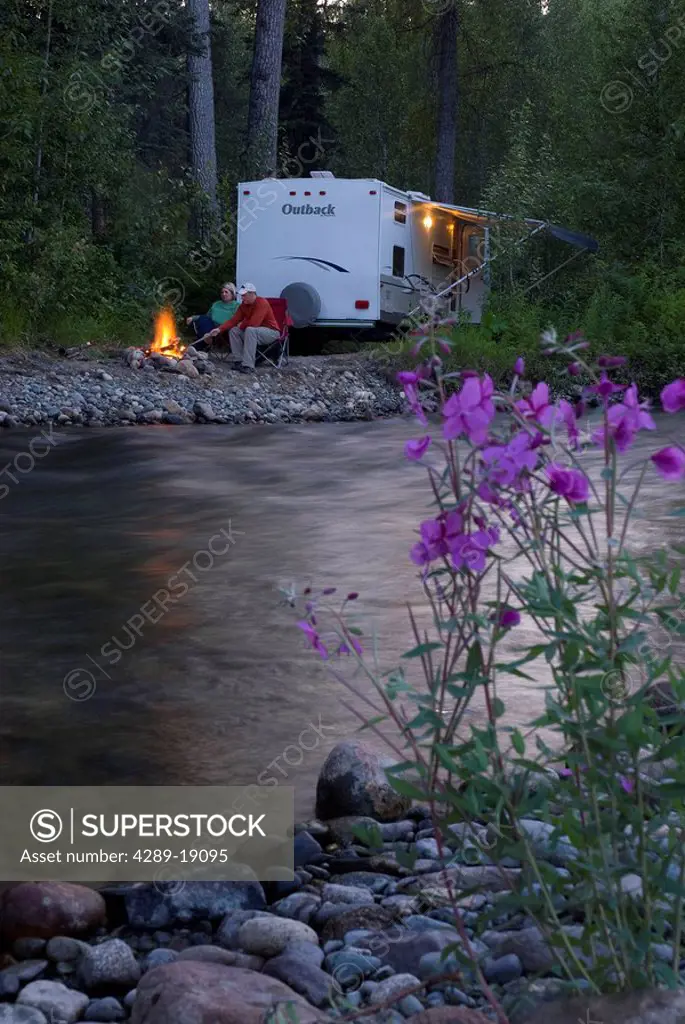 A couple enjoy their campfire near their travel trailer by Montana Creek in Southcentral Alaska