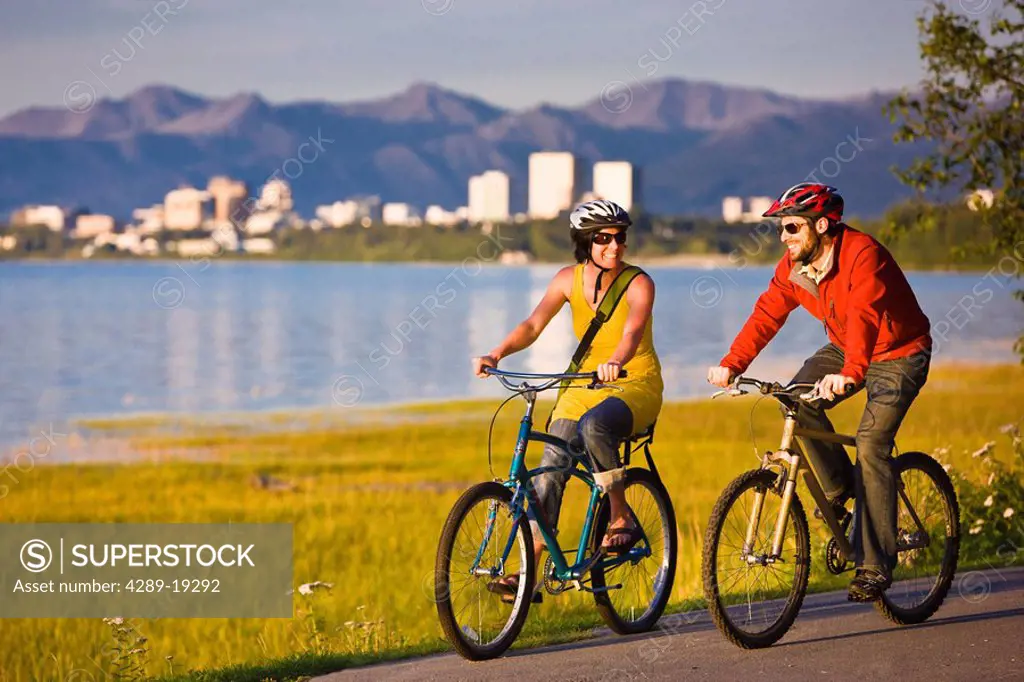 Bicyclists riding on the Tony Knowles Coastal Trail with the Anchorage skyline in the background, Southcentral Alaska
