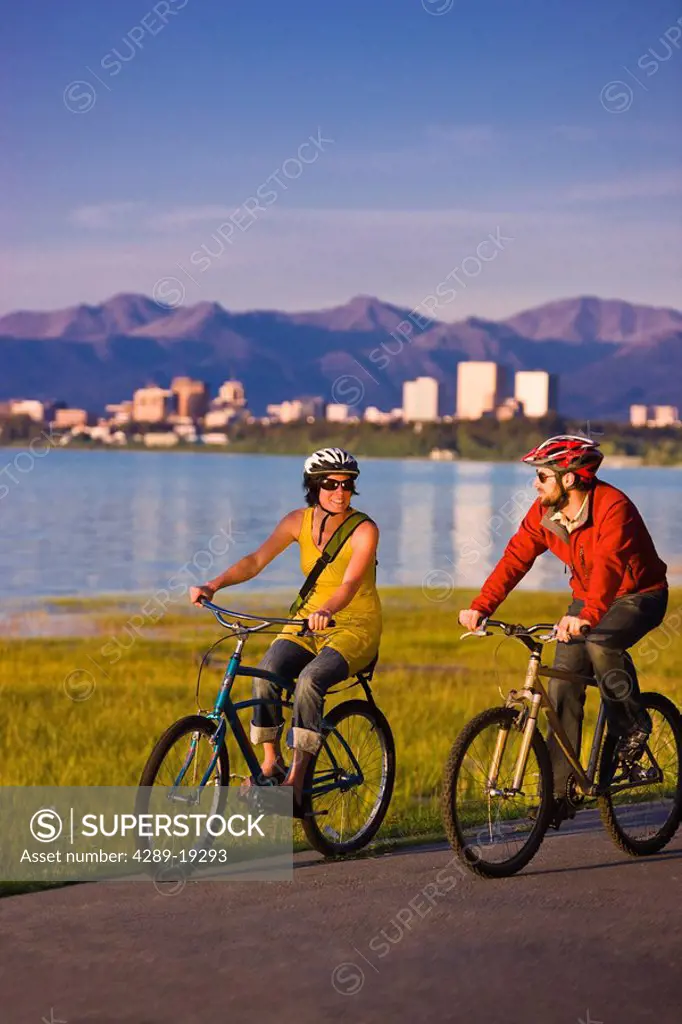 Bicyclists riding on the Tony Knowles Coastal Trail with the Anchorage skyline in the background, Southcentral Alaska