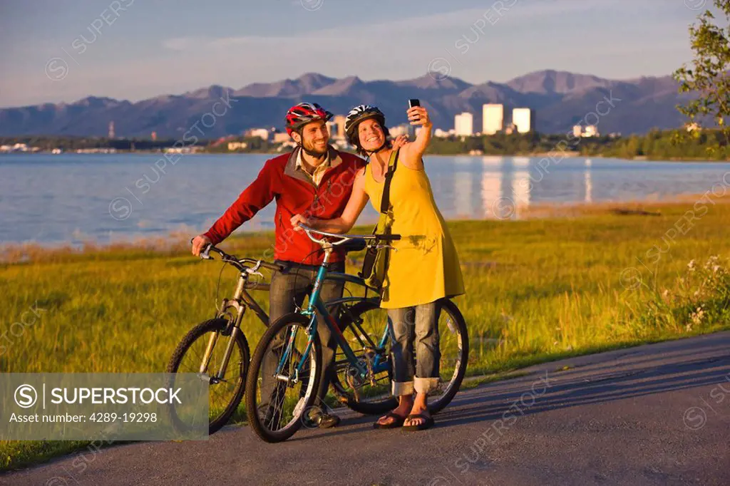 Bicyclists resting and taking self_portraits along the Tony Knowles Coastal Trail with the Anchorage skyline in the background, Southcentral Alaska