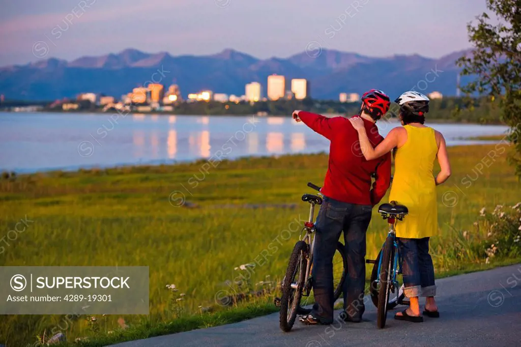 Bicyclists resting and and enjoying the sunset along the Tony Knowles Coastal Trail with the Anchorage skyline in the background, Southcentral Alaska