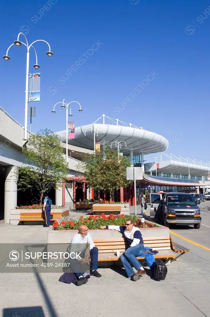 Travelers sitting on bench outside Ted Stevens International Airport Anchorage Alaska Southcentral summer
