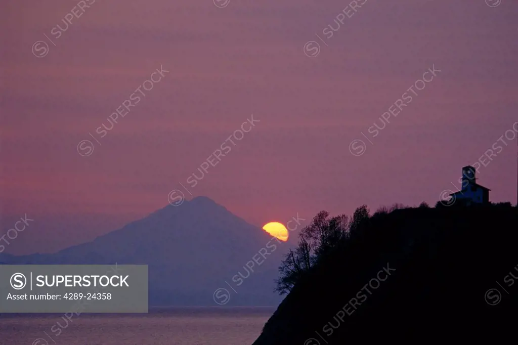 View across Cook Inlet of Mt. Redoubt and a lighthouse at sunset,/nSouthcentral Alaska, Summer