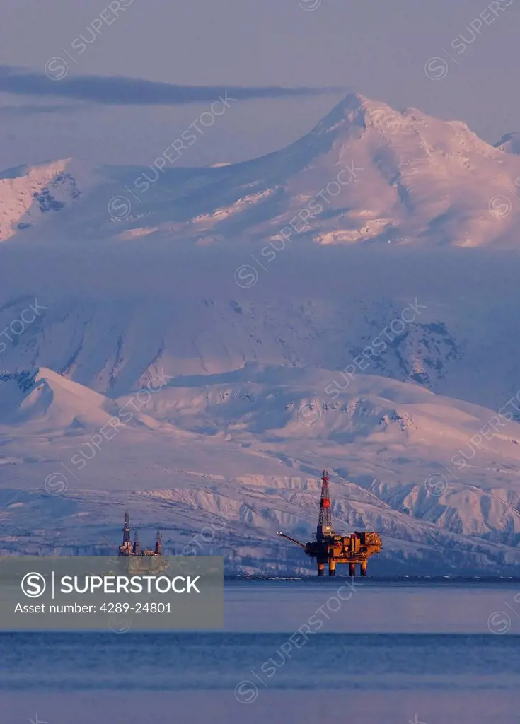 Three drill rigs in Cook Inlet with Mt. Spurr looming large in the background at sunset, Southcentral Alaska, Winter