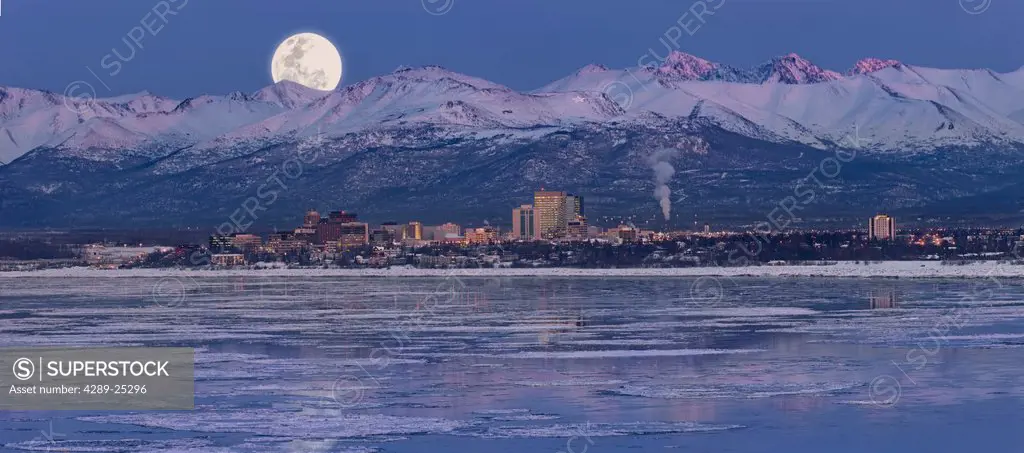 Panoramic view of moon rising over the Anchorage skyline and Chugach Mountains at dusk with fireworks overhead as seen from Point Woronzof, Southcentr...