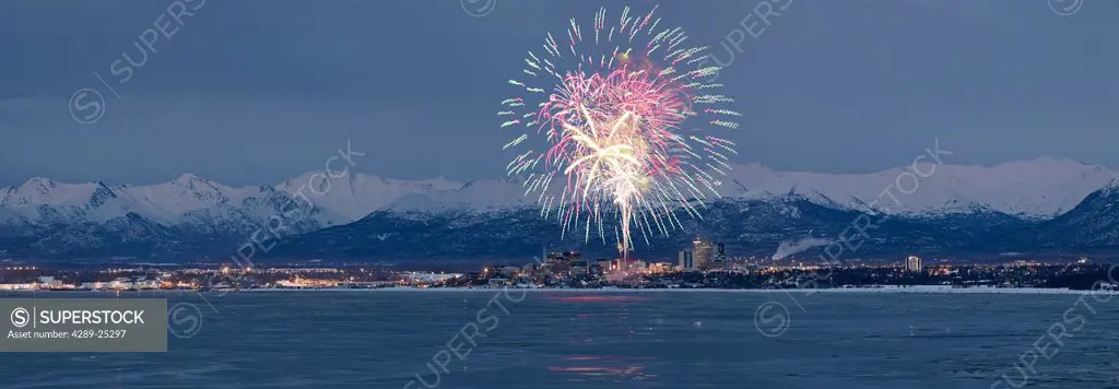 Panormic view of moon rising over the Anchorage skyline and Chugach Mountains at sunset with fireworks overhead as seen from Point Woronzof, Southcent...