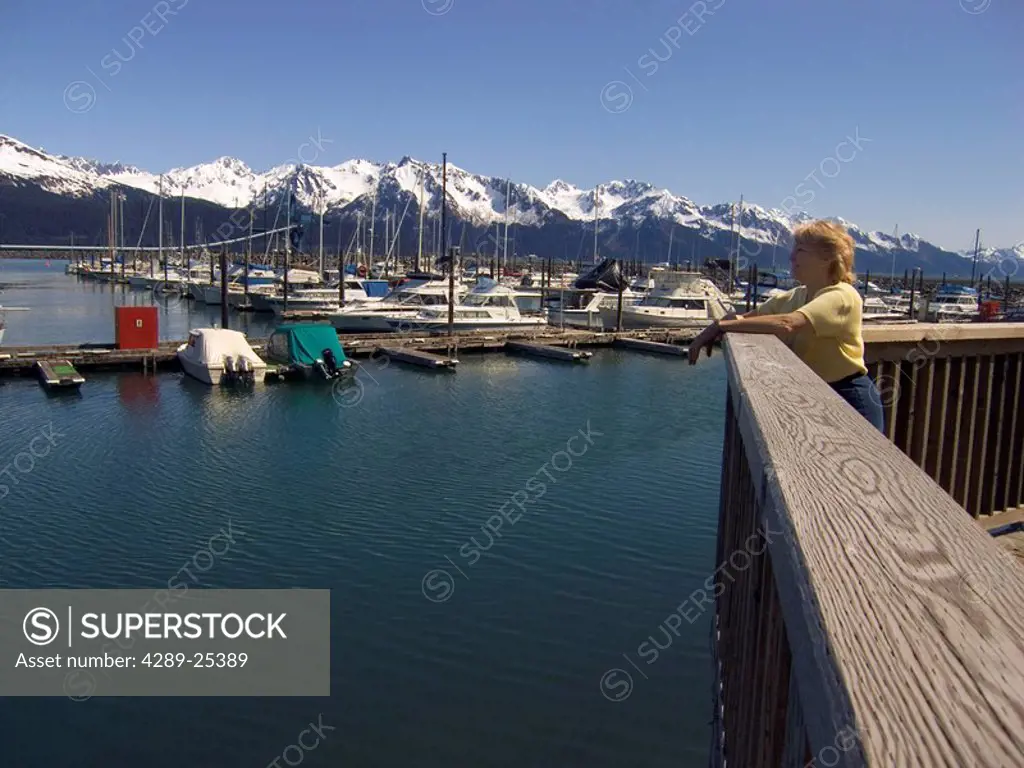 Female visitor standing on boardwalk viewing Seward boat harbor Kenai Peninsula Alaska Summer
