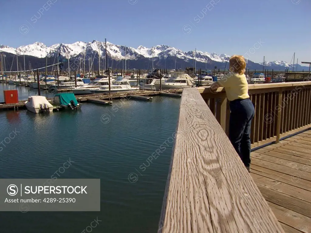 Female visitor standing on boardwalk viewing Seward boat harbor Kenai Peninsula Alaska Summer