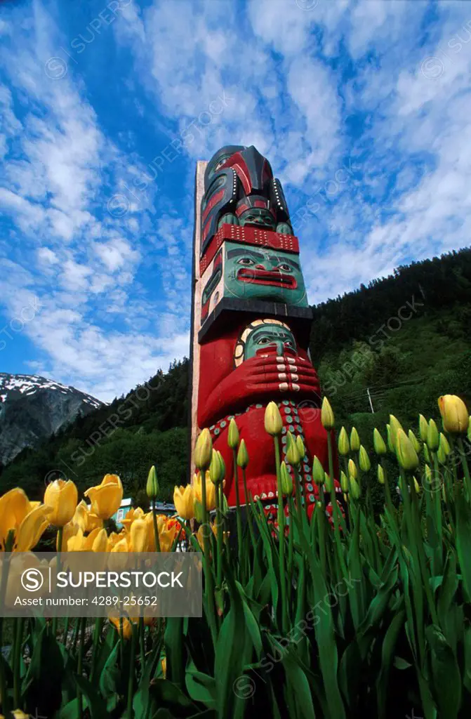 Totem pole with tulips Juneau Southeast Alaska mountains coast summer PR tourist