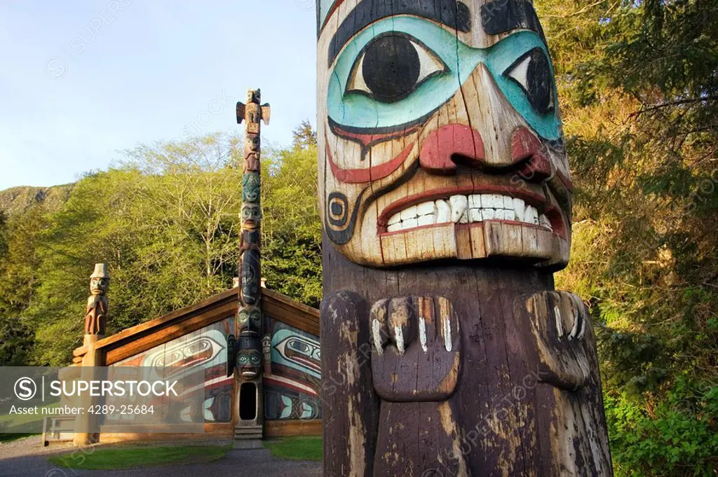 Close up of totem pole with Tribal Clan House in the background at Totem Bight State Historical Park near Ketchikan Alaska Southeast Summer